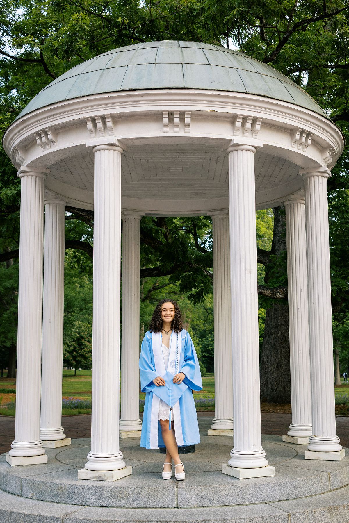 A woman in her graduation robe and stole at the Old Well on UNC's campus in Chapel Hill, NC