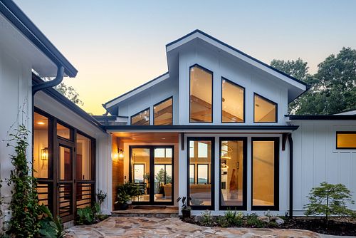 Close up view of exterior entry with large floor to ceiling windows, a covered patio entry, and a view through the house to the lake with the exterior lights off.