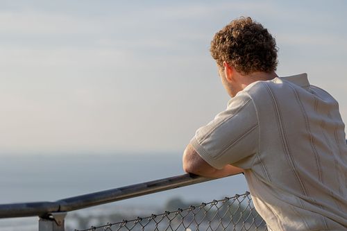 Man i profil som lutar mot räcke och blickar ut över vattnet, redaktionell stil