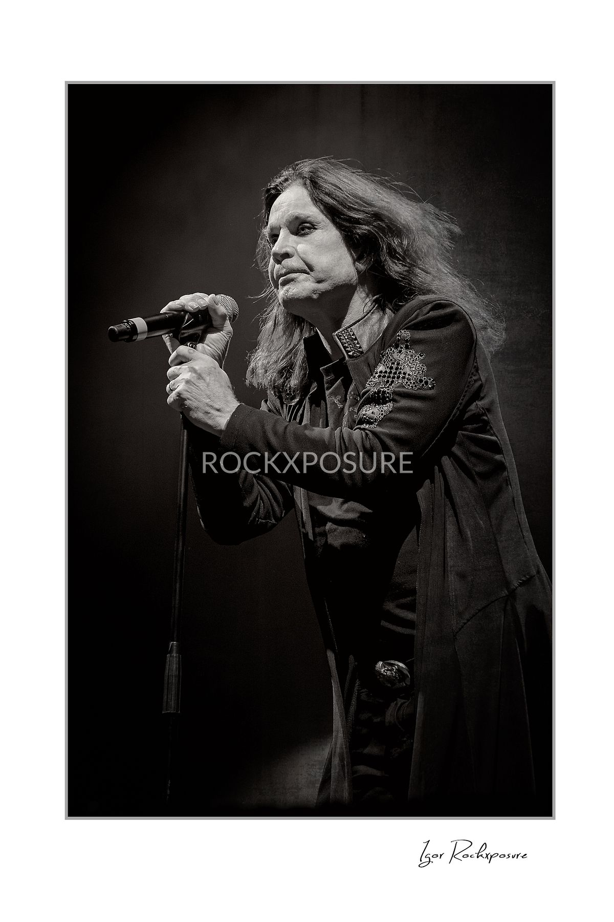 Ozzy Osbourne of Black Sabbath singing into a microphone captured in a dramatic black and white portrait during a live performance