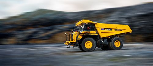 Komatsu HD605 dump truck in motion, captured with motion blur, suitable for a website header