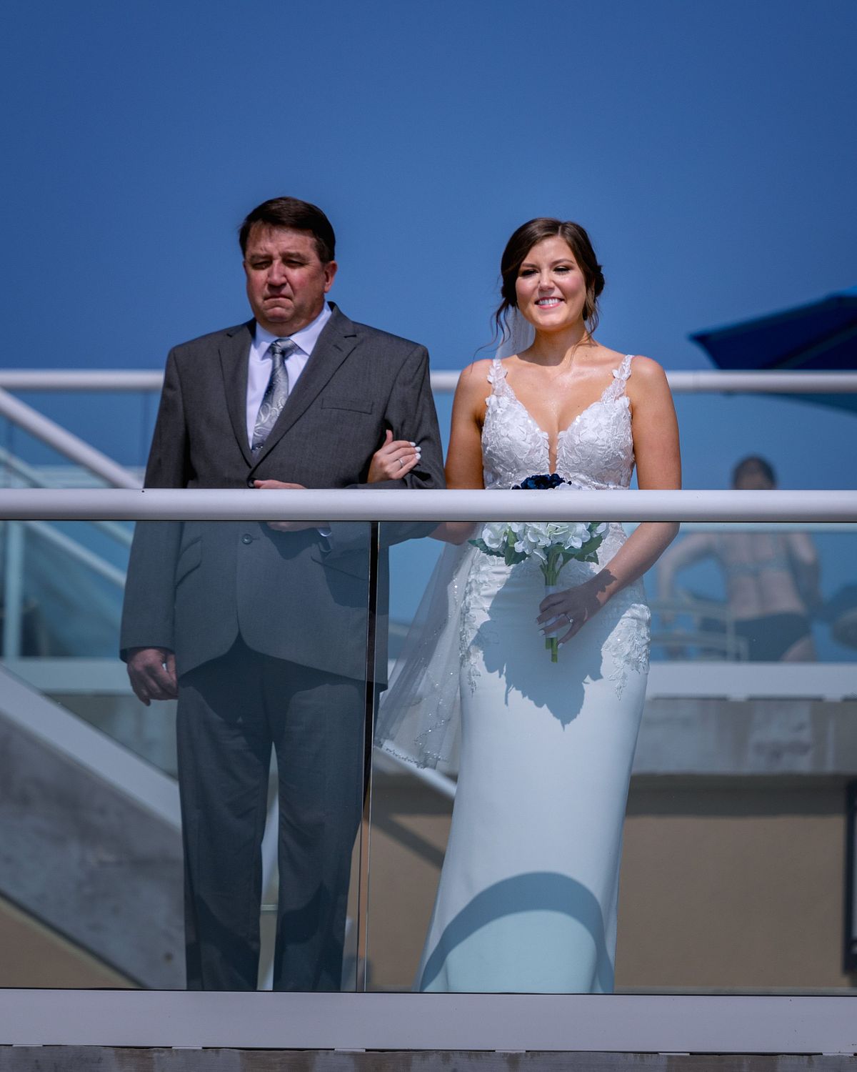 bride and groom overlooking the terrace at the hyatt in dewey beach, the sun is shining hot and the sky is a cool azure blue. the bride is smiling and the dad is emotional