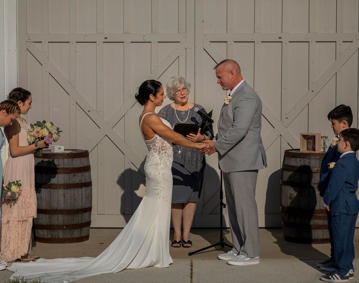 ceremony outside of kylan barn on a warm april day, the bride and groom are holding hands while the officiant reads a poem