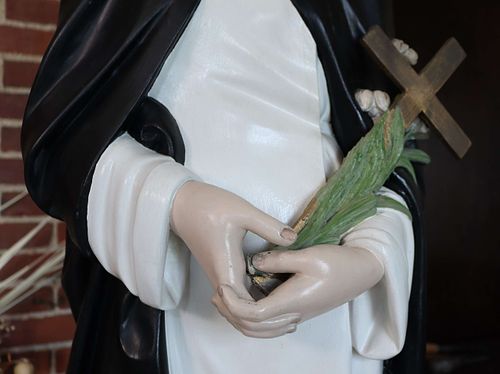 Very pale hands on a statue of St Catherine in need of repainting