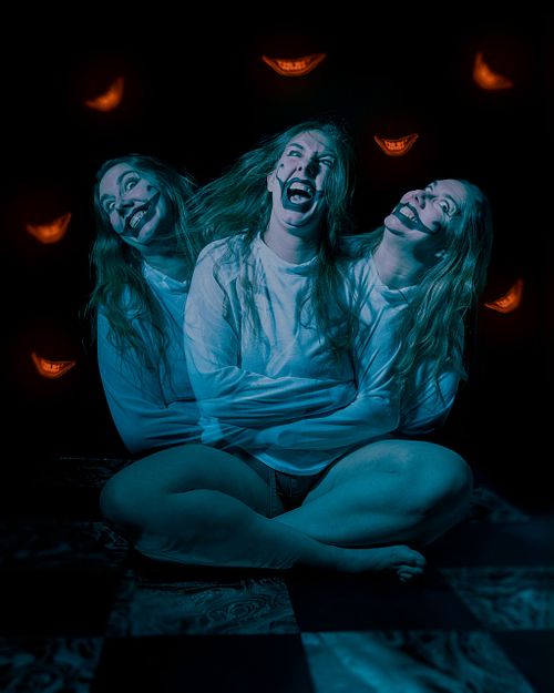 A blue lit scene of a crazy clown woman fighting her straightjacket while orange smiles float all around her.