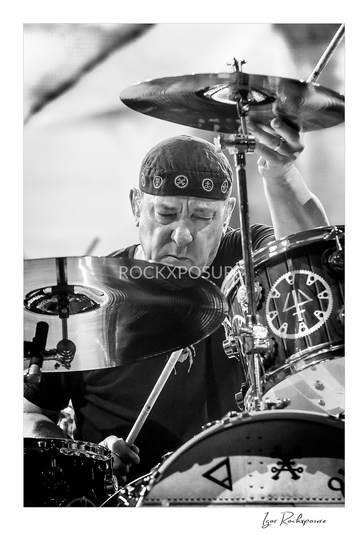 Vertical concert photography of Neil Peart playing drums in black and white photography surrounded by cymbals under stage lighting