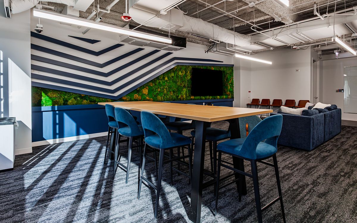 Modern Chicago office collaboration area for Supernova Technology featuring a long wood high-top table, blue velvet bar stools, a biophilic moss wall, and industrial exposed ceilings.