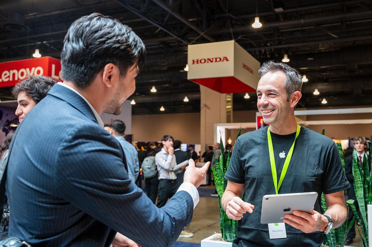 Corporate event photography capturing an Apple team member smiling and speaking with an attendee at the Apple booth during a conference networking event, emphasizing authentic professional connection and meaningful brand engagement.
