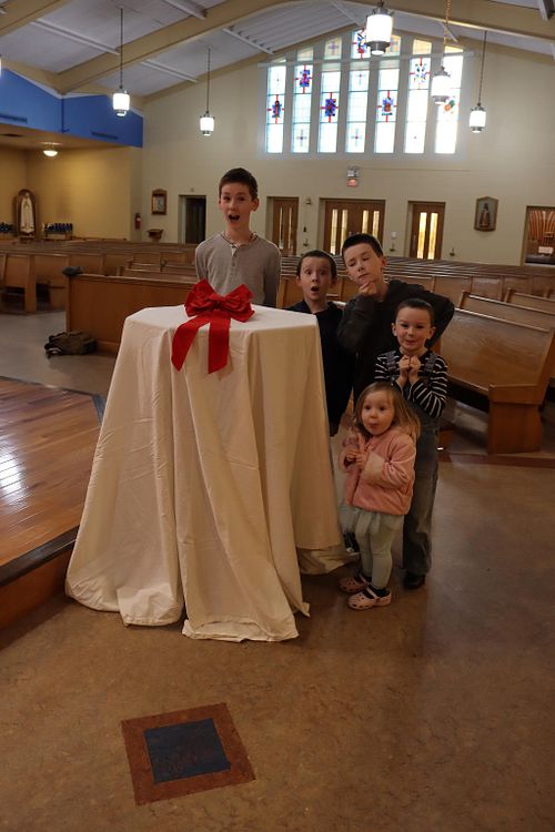 New baptismal font is veiled and ready to show Father Tyron Tomson.  It is surrounded by excited Baker children