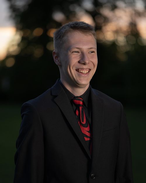 Grad photo of a PACI student in his suit during sunset with a big smile on his face.