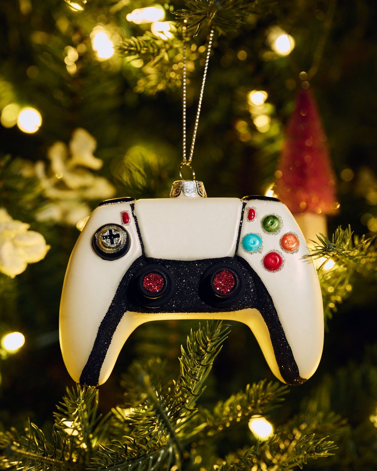 A game controller Christmas ornament hanging on a lit tree.