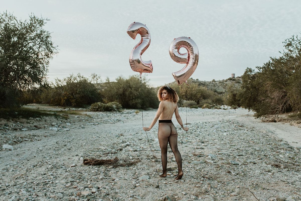 Bold outdoor boudoir photo featuring a woman in fishnets holding birthday balloons, confidently posing in a rugged Arizona desert wash — playful, powerful, and unapologetic.