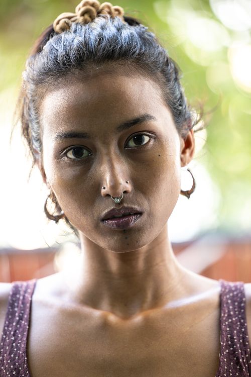 A headshot of an Indian woman wearing earrings and a nose ring, dressed in a purple top.