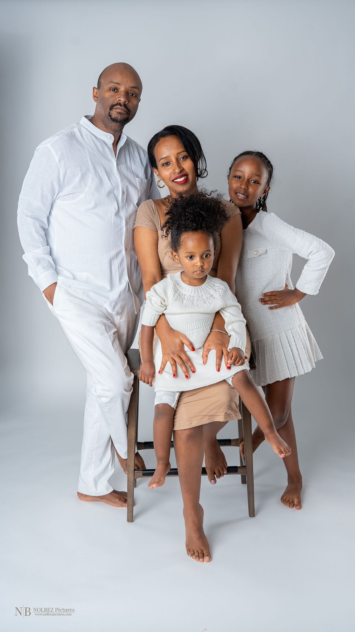 A studio family portrait of a couple with their two daughters wearing white clothes