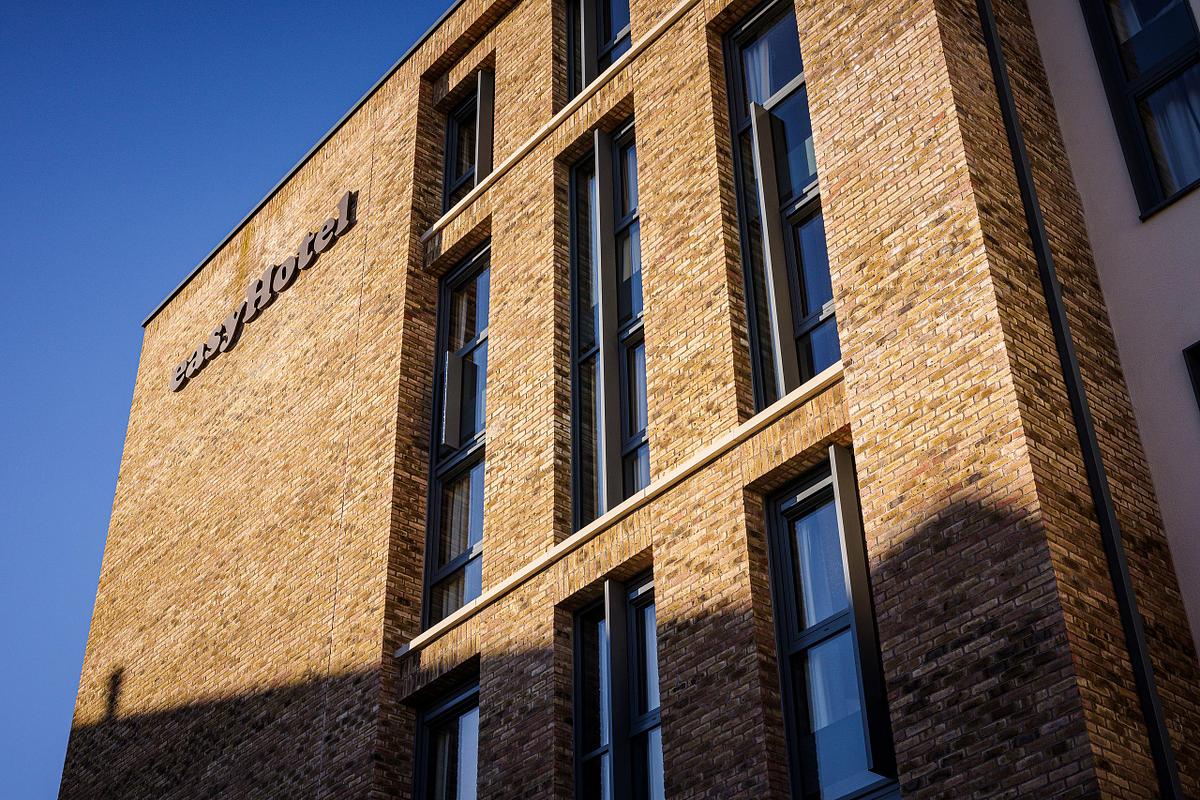 Exterior view of the Easy Hotel Dublin, showcasing its modern brick facade and tall, narrow windows. The 'easyHotel' logo is visible on the building. Clear blue sky in the background.