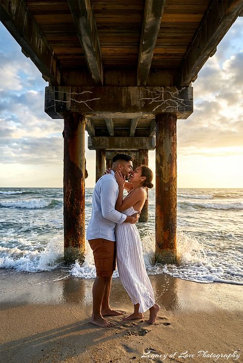 An intimate kiss after a surprise sunset beach proposal under a wooden pier in Jacksonville, captured by Legacy of Love Photography.