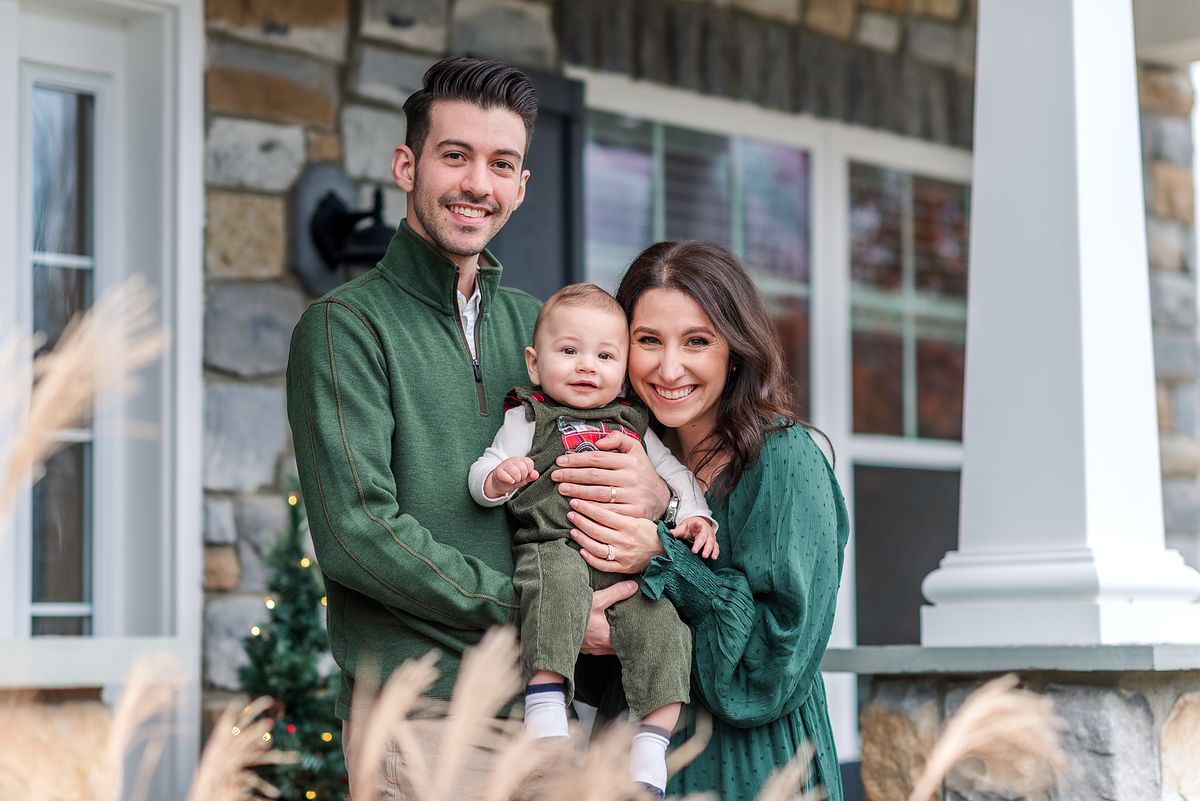 Husband and wife dressed in green Christmas attire holding their baby and smiling with Cranberry Township, PA newborn photographer