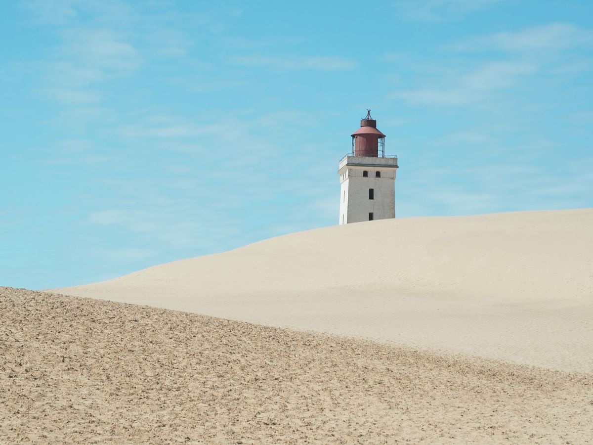 Faro solitario che emerge dal deserto danese in estate, illuminato dal sole caldo, simbolo di quiete e isolamento