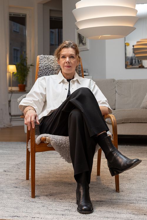 Person sittande i fåtölj i ett skandinaviskt vardagsrum med modern taklampa och mjuka texturer.