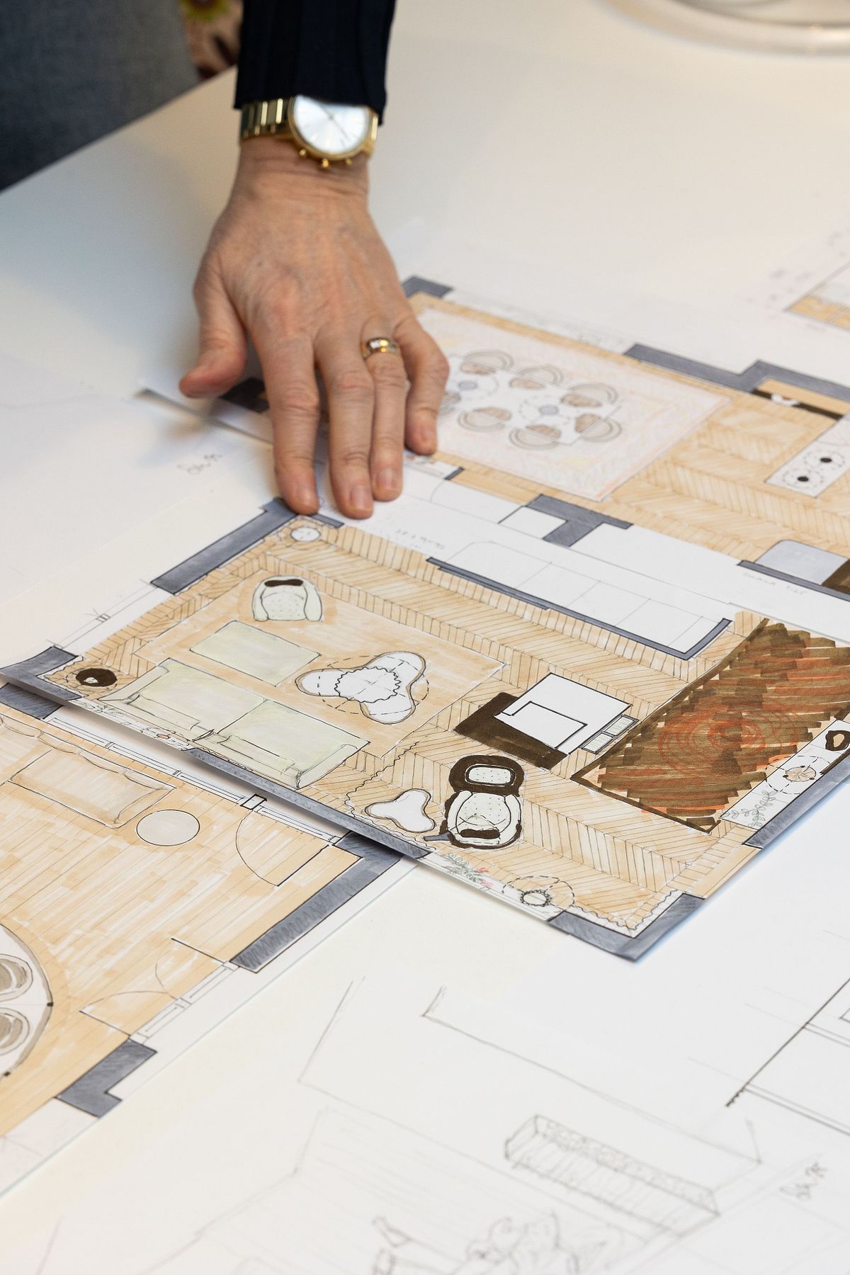 Hand som pekar p&aring; en f&auml;rglagd inredningsplan med m&ouml;blering och rumslayout p&aring; bord.