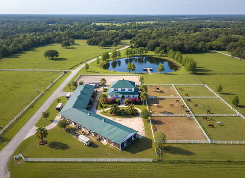 Aerial drone photography of a luxury equestrian estate with a private pond, large main residence, and stables, captured by PrimePropertyPhoto in Gainesville, FL.