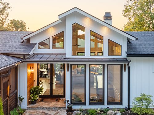 Close up view of exterior entry with large floor to ceiling windows, a covered patio entry, and a view through the house to the lake.