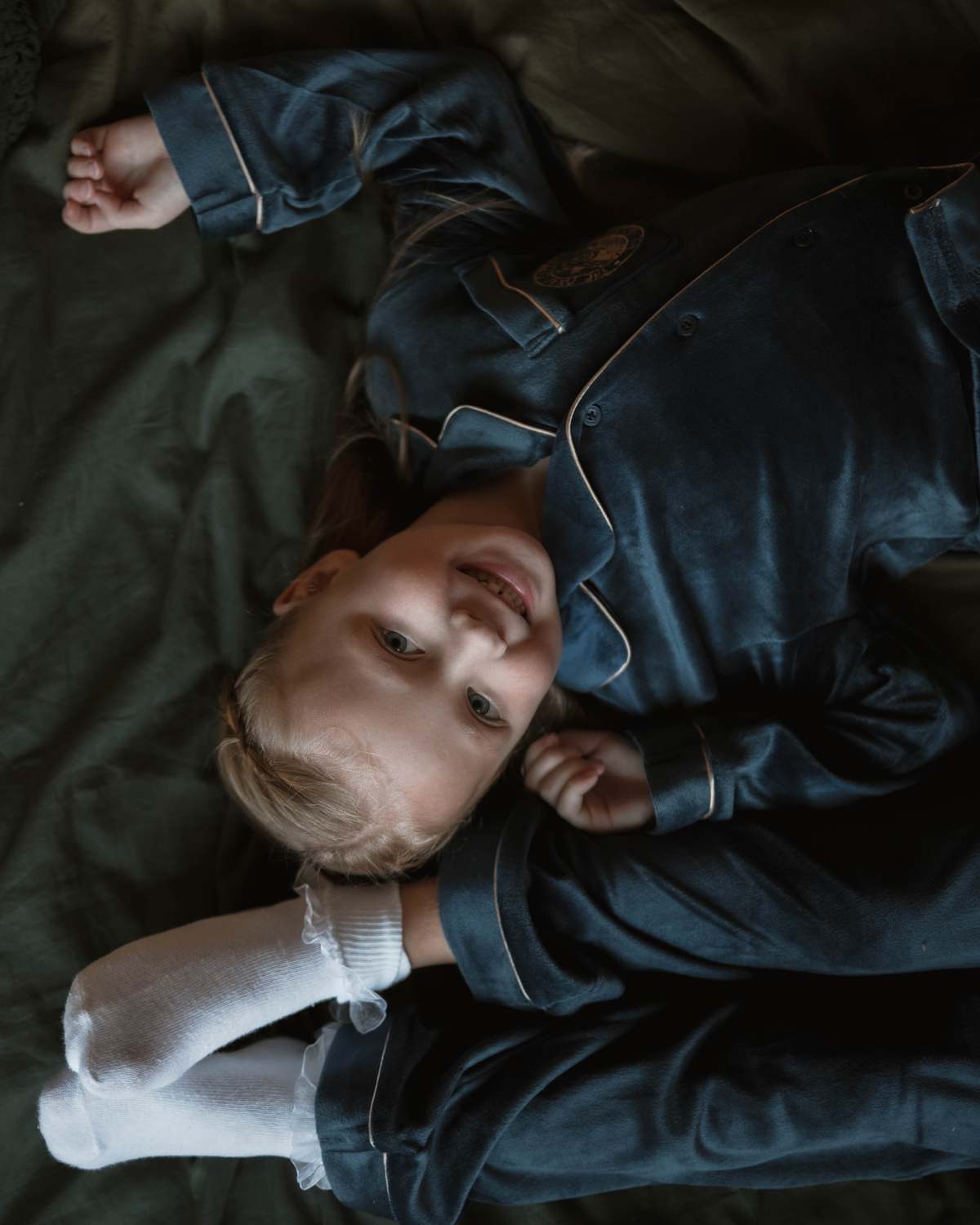 Child lying down in dark PJ outfit, editorial childrenswear campaign photography