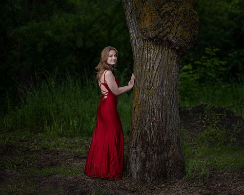 High School Grad standing in the trees in her red gown.