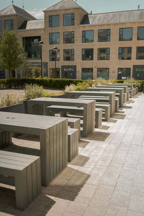 Outdoor seating area with tables and chairs arranged in a shared courtyard between buildings