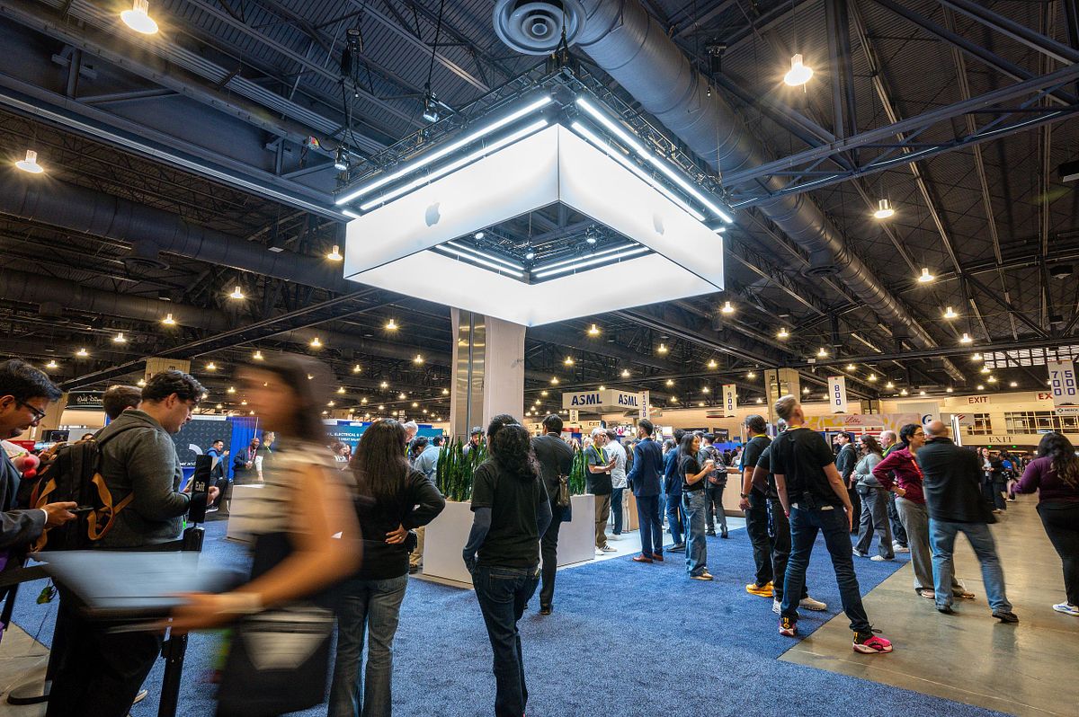 Corporate event photography capturing attendees gathered around the illuminated Apple booth at a large-scale professional conference in Philadelphia, highlighting brand engagement, innovation, and dynamic community interaction.