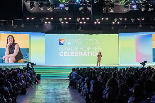 Brenda Darden Wilkerson speaking on the main stage at Grace Hopper Celebration 2024 in Philadelphia, with full audience and event branding illuminated behind her, captured by professional event photographer.