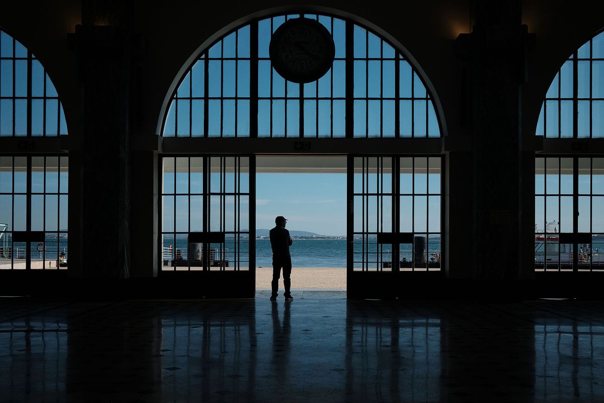 A silhouette of a person standing in a grand hall with arched windows overlooking the sea, captured by photographer Sandeep Gajula