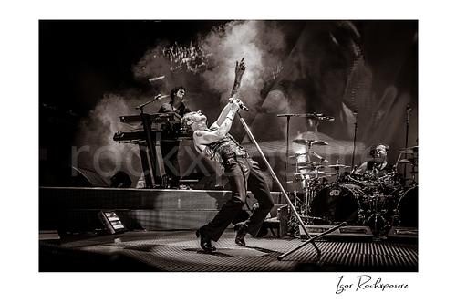 Horizontal B&W image of Depeche Mode members Peter Gordeno, Dave Gahan, and Christian Eigner performing on stage