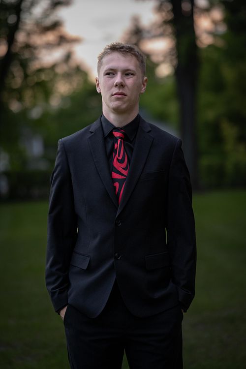 Photo of Prince Albert Grad in a suit standing in PACI's school grounds at sunset.