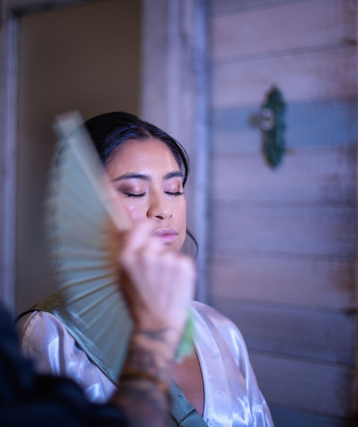 A close-up bridal portrait at Kylan Barn featuring moody, low-key lighting as a bride gets ready with a handheld fan.