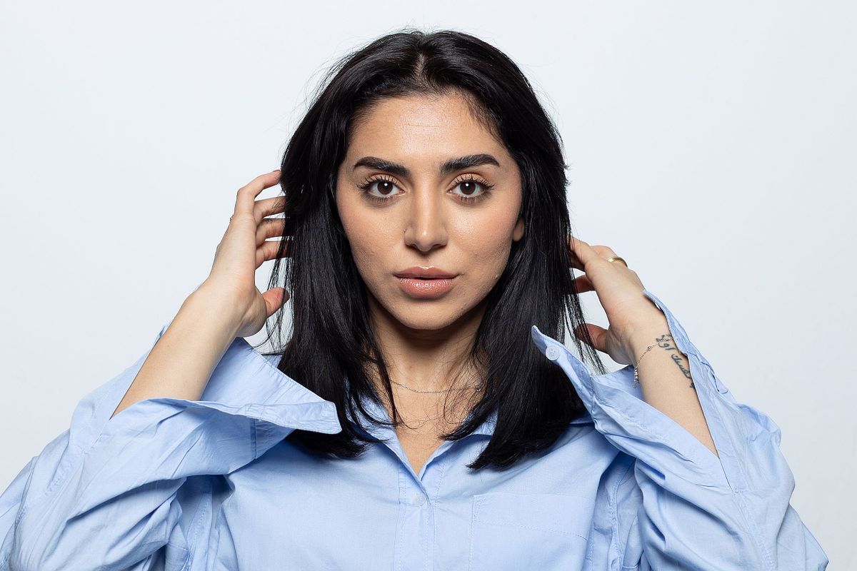 Person i ljusbl&aring; skjorta tittar rakt in i kameran med h&auml;nderna n&auml;ra h&aring;ret, vit bakgrund, Stockholm