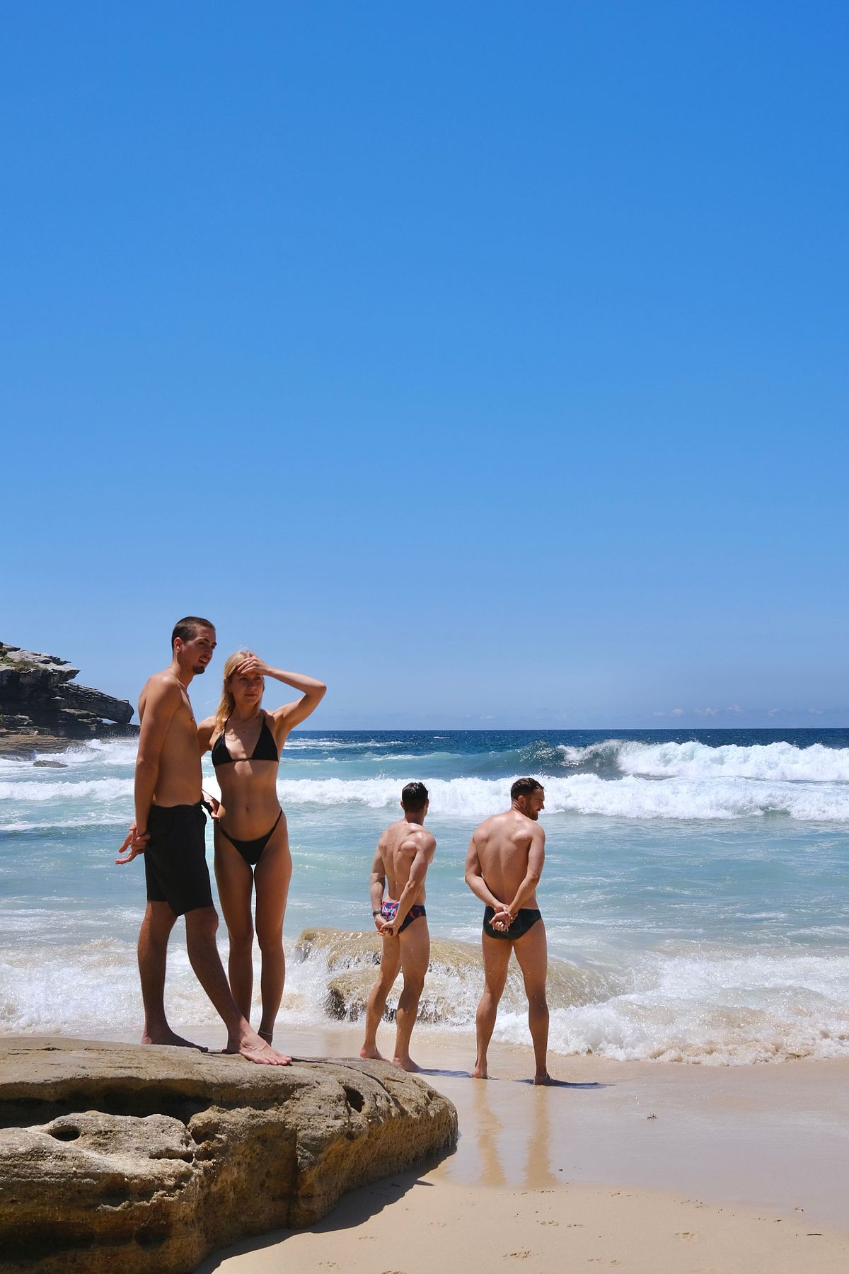 A couple on the beach with what looks like "speedo bodyguards" in Sydney, Australia