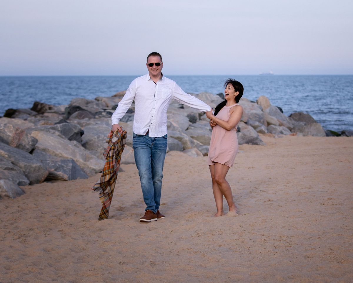 couple being playful on the beach during engagement session at cape henlopen, de.