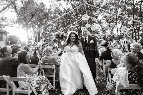 A bride and groom celebrate as they walk out of their ceremony to guests cheering them on