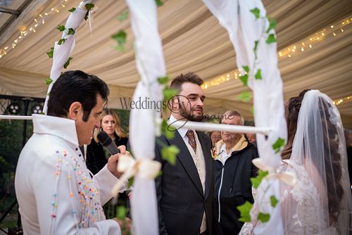 A vicar dressed like Elvis speaking to the bride and groom during their wedding ceremony, captured by Weddings By Jermaine.