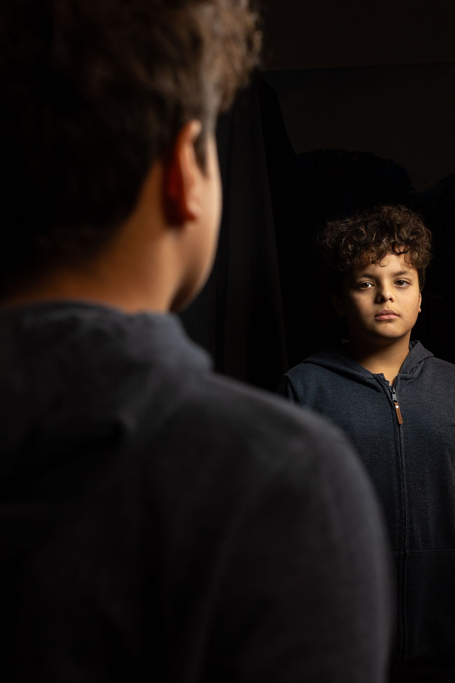 Young boy looking into mirror with serious expression, conceptual portrait photography in Stockholm