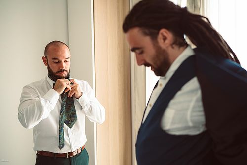 "testimone che si allaccia la cravatta mentre lo sposo indossa la giacca"