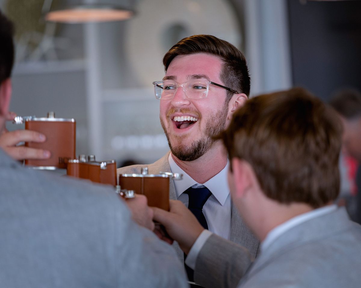 a happy groom is toasting his groomsmen with a whiskey flask at the hyatt in dewey beach