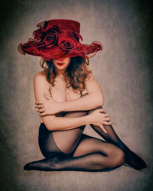 Photographie fine art d&rsquo;une femme assise nue en collants noirs, coiff&eacute;e d&rsquo;un large chapeau rouge &agrave; fleurs, dans une posture repli&eacute;e m&ecirc;lant pudeur et sensualit&eacute; &mdash; &oelig;uvre de Pascal Yennis, Namur, Belgique.