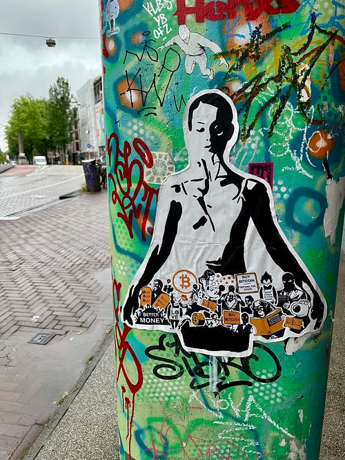 Street art by Street Cyber featuring a black and white stencil of a figure with a skirt composed of various Bitcoin-themed protest signs and figures. Signs read "BETTER MONEY," "BUY BITCOIN," and depict diverse individuals advocating for financial freedom. This piece, in signature stencil style, symbolizes the grassroots movement for decentralized finance and challenges traditional economic systems. A powerful urban commentary on social change and Bitcoin's potential. #Bitcoin #StreetArt #BetterMoney #FinancialFreedom #Decentralization #CryptoArt #UrbanArt #StencilArt #SocialChange #StreetCyberArt #ArtForChange #Grassroots #EconomicRevolution