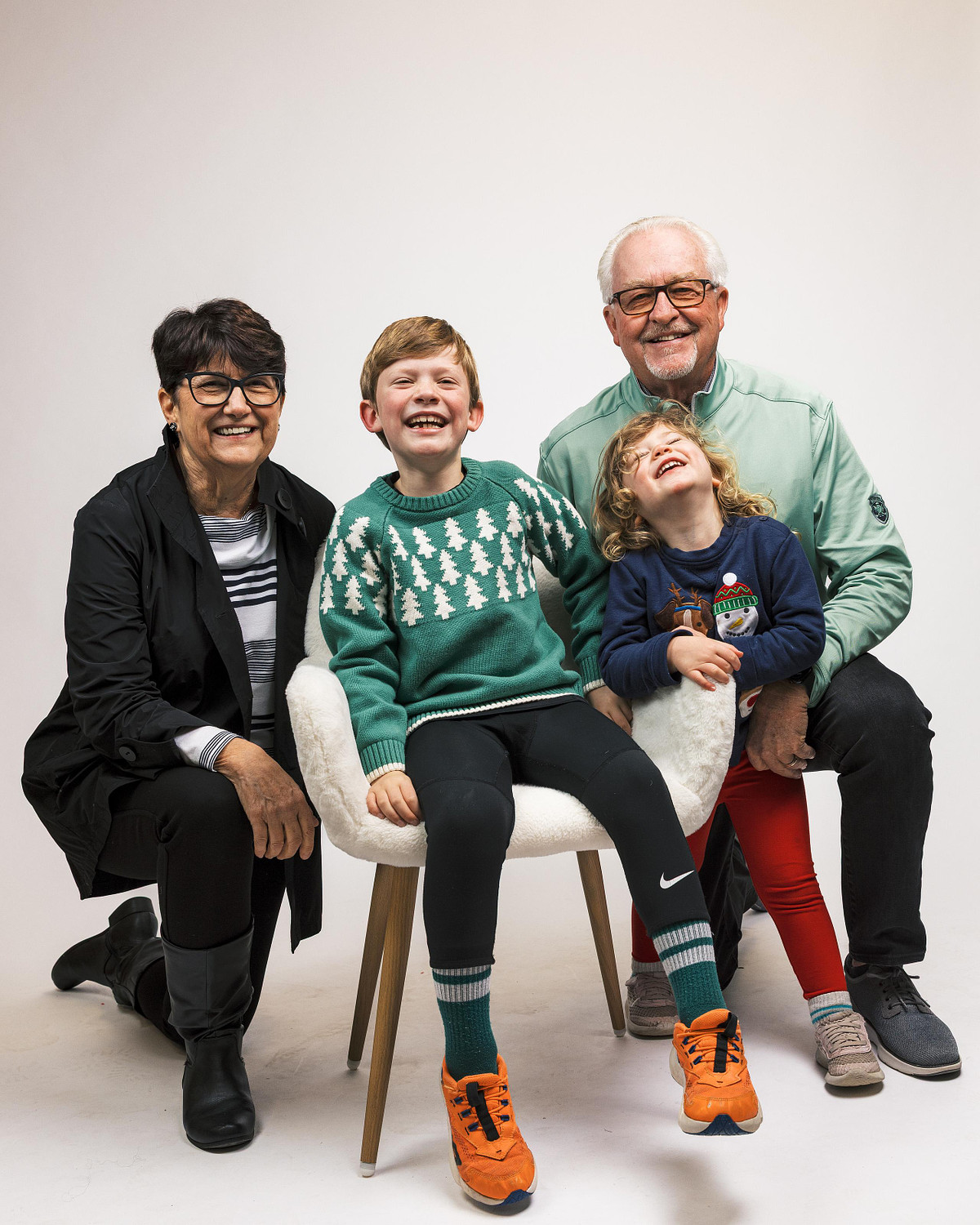A multigenerational family portrait featuring grandparents and grandchildren laughing together in a white studio setting.