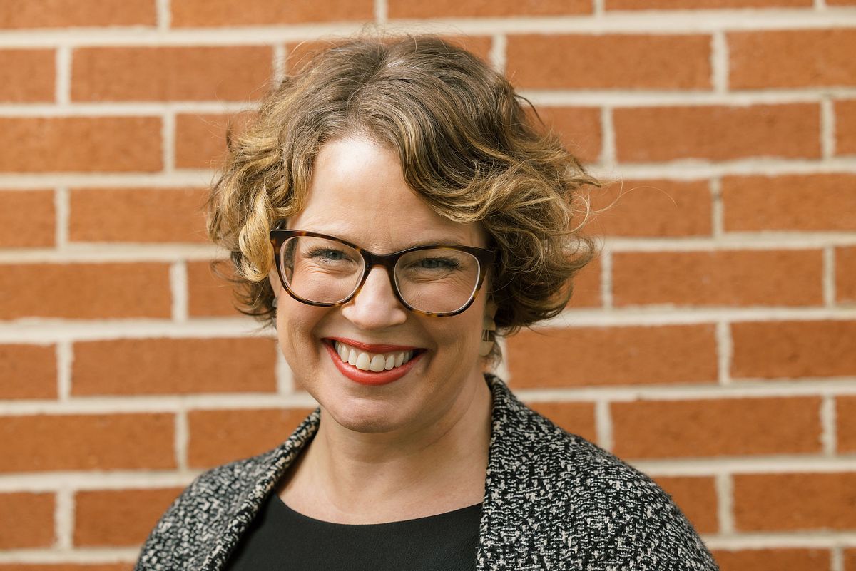 A close-up headshot a woman against a brick backdrop at an outdoor location in Carrboro, NC