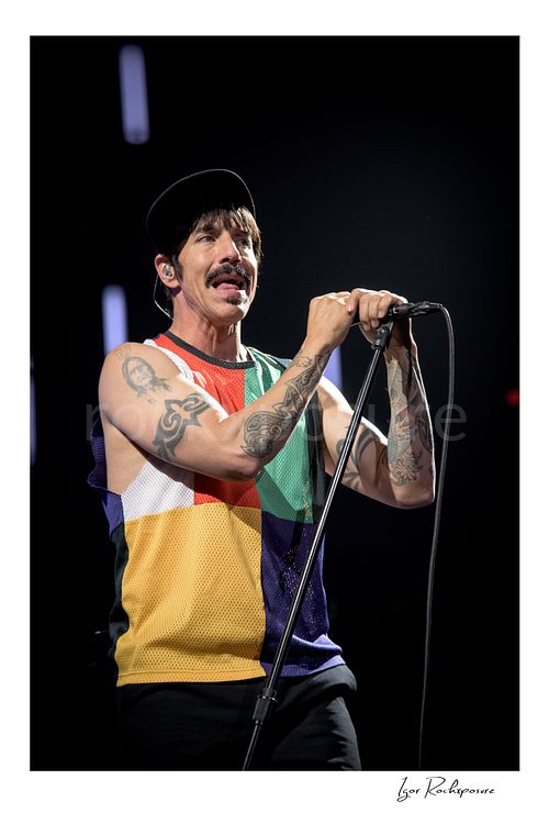 Anthony Kiedis Red Hot Chili Peppers Live Concert Print  Vertical color image of Anthony Kiedis of Red Hot Chili Peppers singing at the microphone in a close live performance portrait, wearing a multicolor sleeveless top and black cap against a dark stage background
