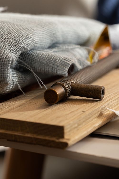 Närbild av ett mörkt metallbeslag på träprov med tygprover i bakgrunden, som del av inredningsdesign och materialval.