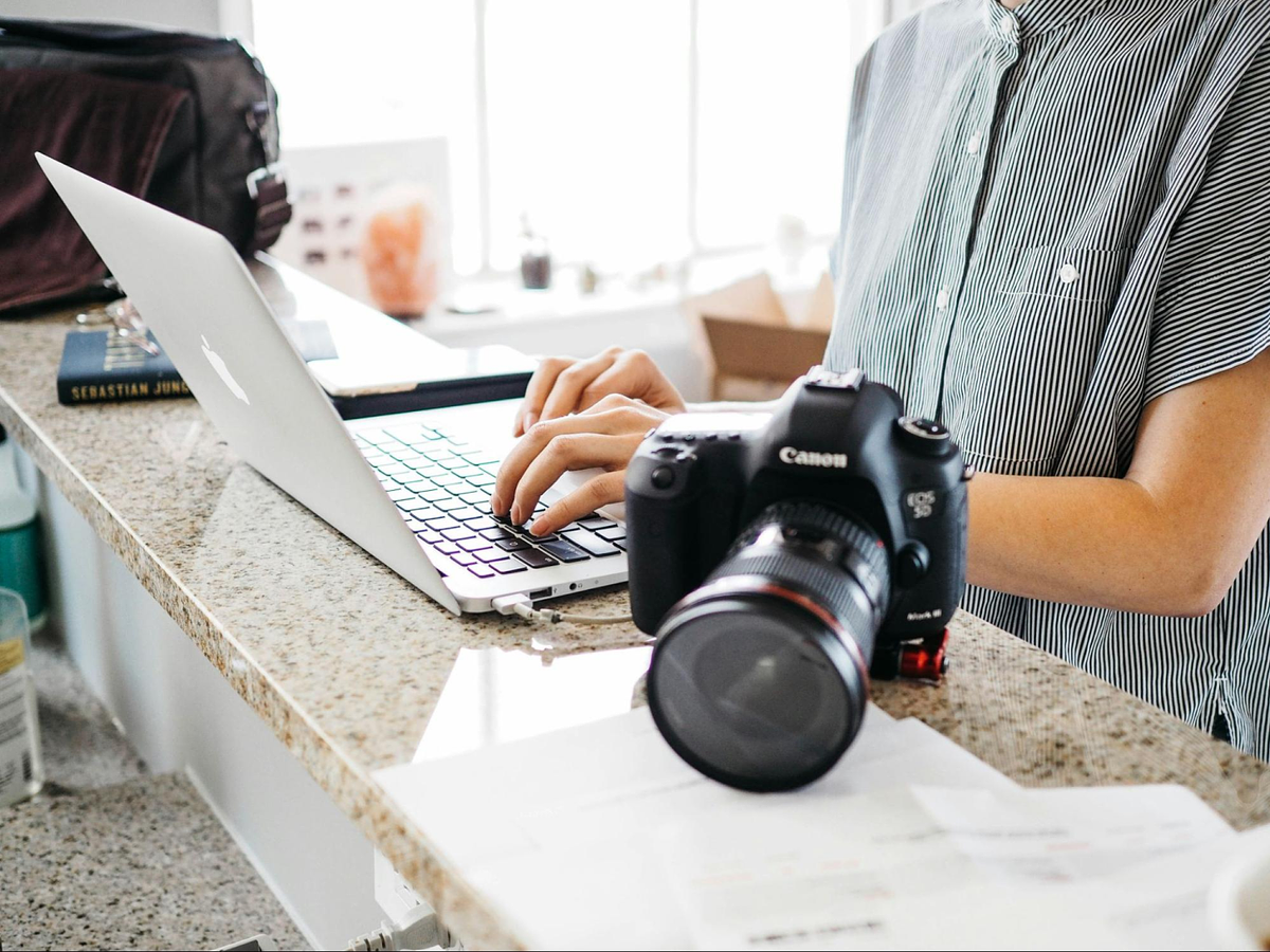 una persona che digita sulla tastiera di un computer portatile con una macchina fotografica Canon sopra il tavolo di marmo